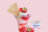 A strawberry parfait in a tall glass with whipped cream and strawberries, served next to a container of strawberry Nutricrem.